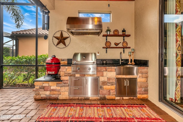 view of patio with a sink, glass enclosure, a grill, and an outdoor kitchen