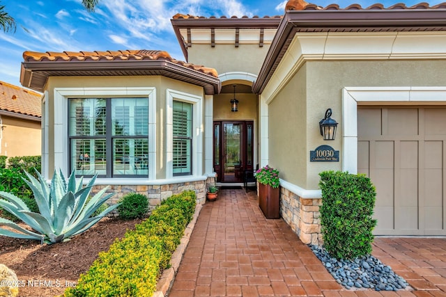 doorway to property with stucco siding, stone siding, an attached garage, and a tile roof