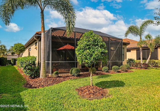 rear view of property with stucco siding, a lawn, a lanai, and a tile roof