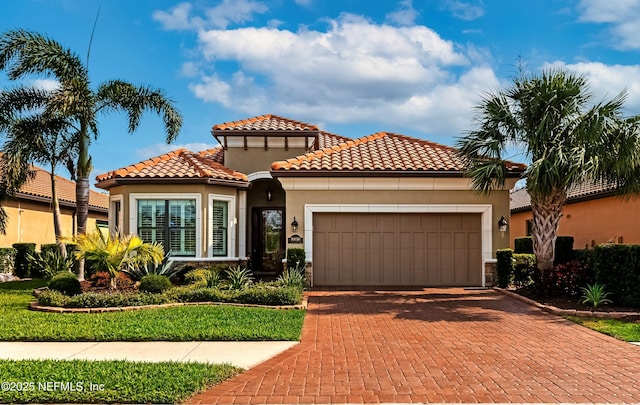 mediterranean / spanish house with stucco siding, a tile roof, decorative driveway, and a garage