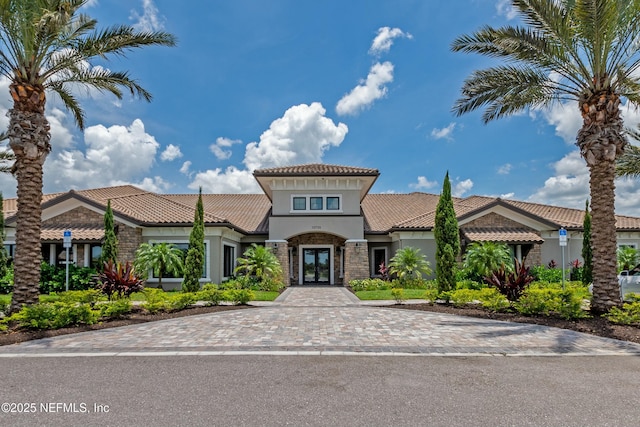 view of front of property featuring a tiled roof, french doors, stone siding, and stucco siding