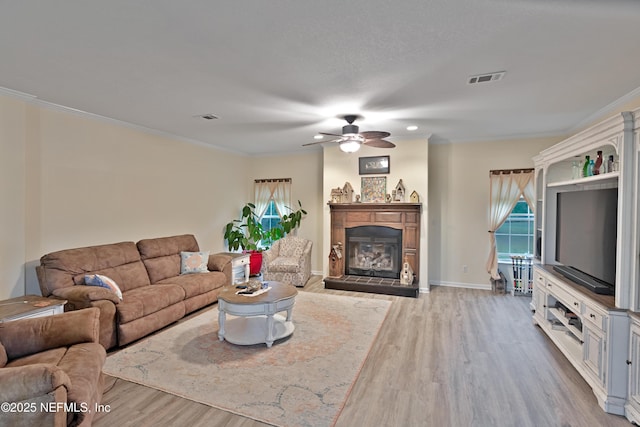 living room featuring a glass covered fireplace, crown molding, visible vents, and wood finished floors