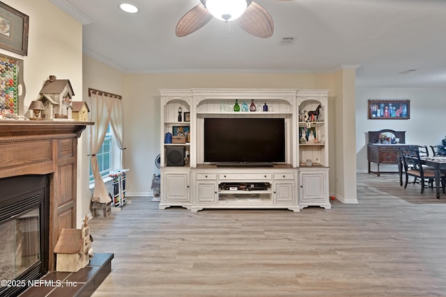 living room with a glass covered fireplace, crown molding, visible vents, and light wood finished floors