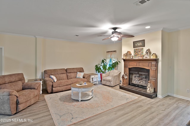 living room featuring wood finished floors, visible vents, baseboards, a tiled fireplace, and crown molding