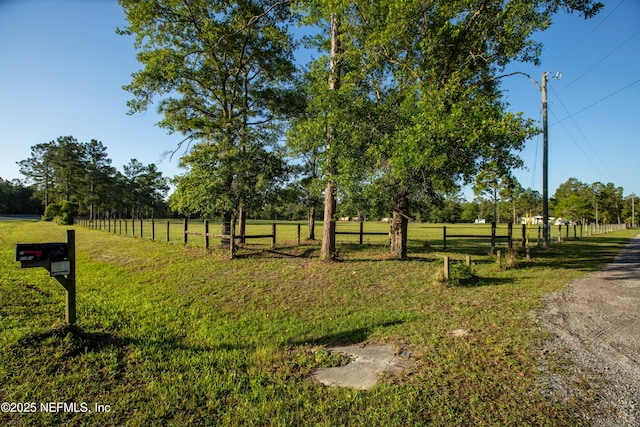 view of community featuring a rural view, a yard, and fence