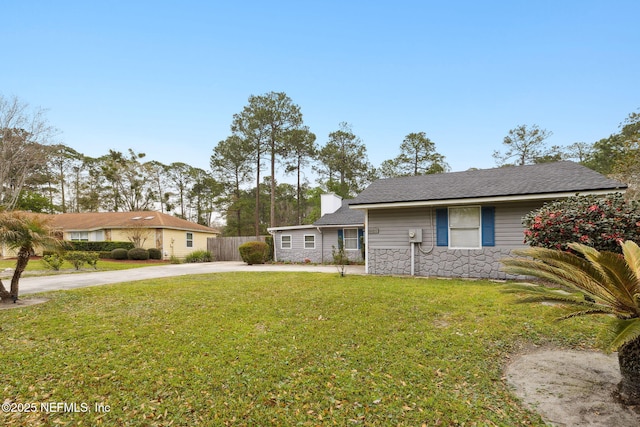 view of front of home featuring stone siding, concrete driveway, a front lawn, and fence