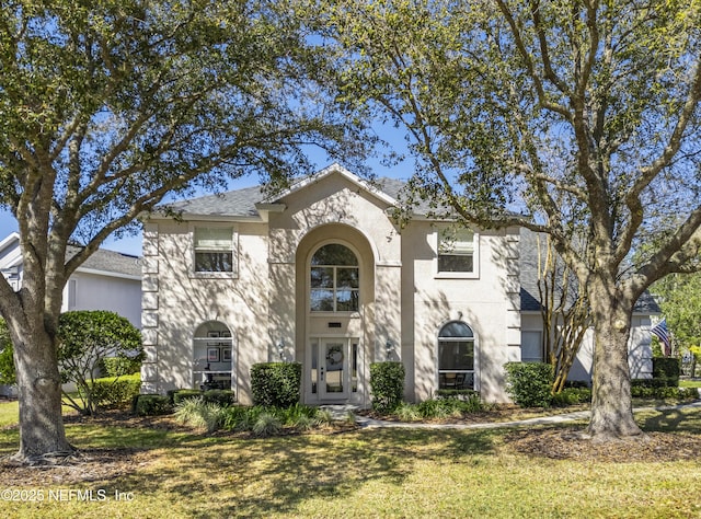 view of front of house with roof with shingles, a front yard, and stucco siding