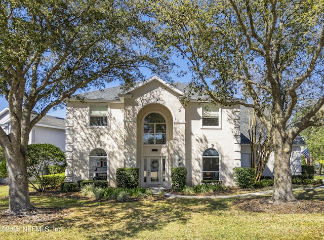 traditional-style home with a shingled roof, a front yard, and stucco siding