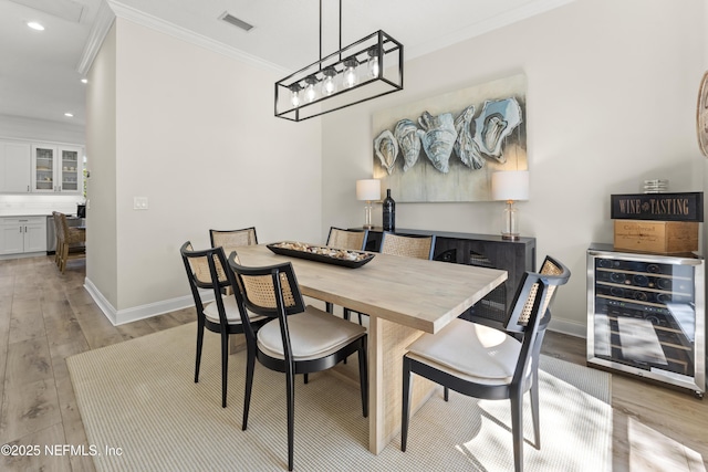 dining space featuring visible vents, crown molding, baseboards, wine cooler, and light wood-style flooring