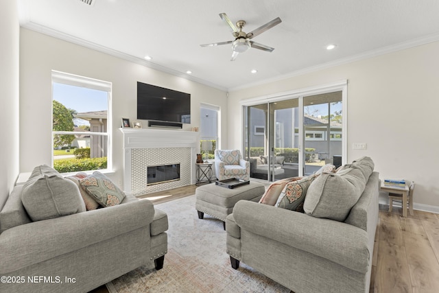 living room featuring a wealth of natural light, crown molding, a tiled fireplace, and light wood-type flooring