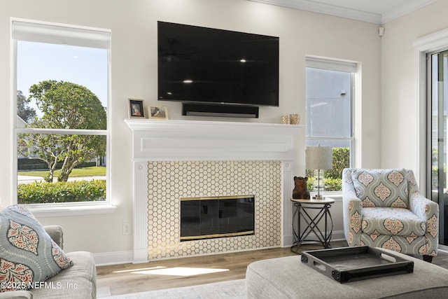 living area with a tiled fireplace, wood finished floors, baseboards, and ornamental molding