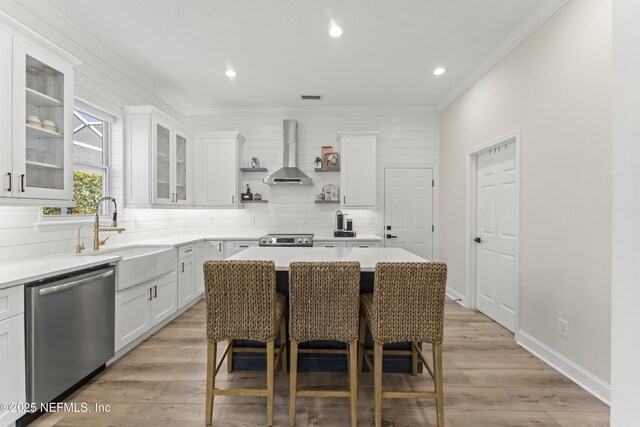 kitchen featuring a sink, white cabinetry, appliances with stainless steel finishes, crown molding, and wall chimney range hood