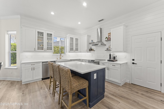 kitchen with a sink, stainless steel appliances, white cabinets, and wall chimney range hood