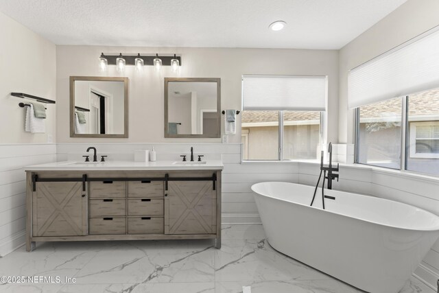 bathroom with a sink, a freestanding bath, marble finish floor, and wainscoting