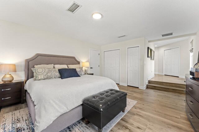 bedroom featuring visible vents, two closets, baseboards, and wood finished floors