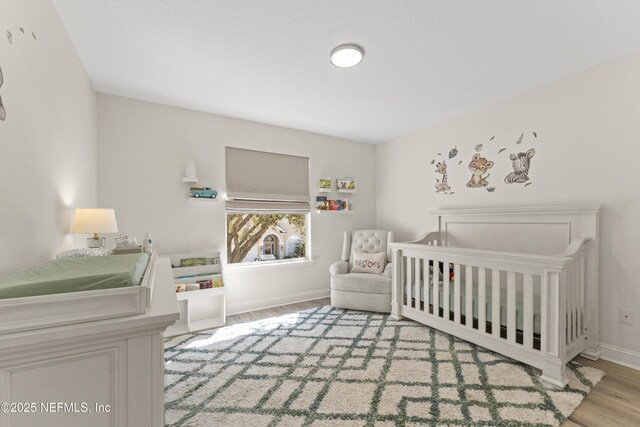 bedroom featuring baseboards, a nursery area, and wood finished floors