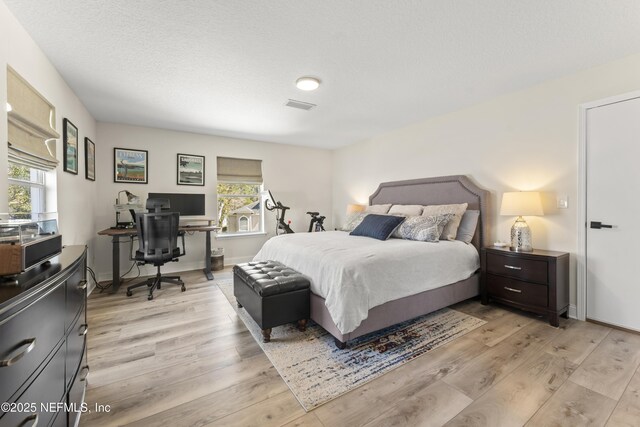 bedroom with a textured ceiling, light wood-style floors, visible vents, and baseboards