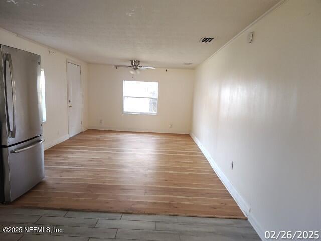 unfurnished room with baseboards, wood finished floors, visible vents, and ceiling fan