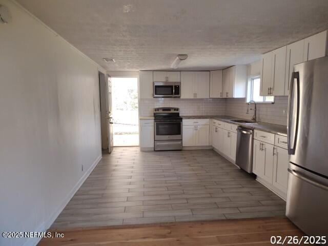 kitchen featuring tasteful backsplash, appliances with stainless steel finishes, light wood-style floors, and a sink