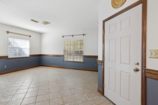 empty room with light tile patterned floors, visible vents, a wealth of natural light, and a textured ceiling