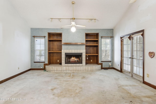 unfurnished living room with baseboards, carpet floors, ceiling fan, track lighting, and a brick fireplace