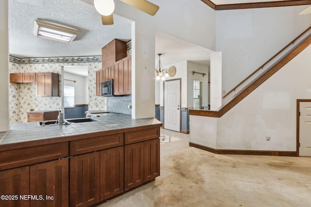 kitchen featuring a sink, a textured ceiling, black microwave, baseboards, and tile counters