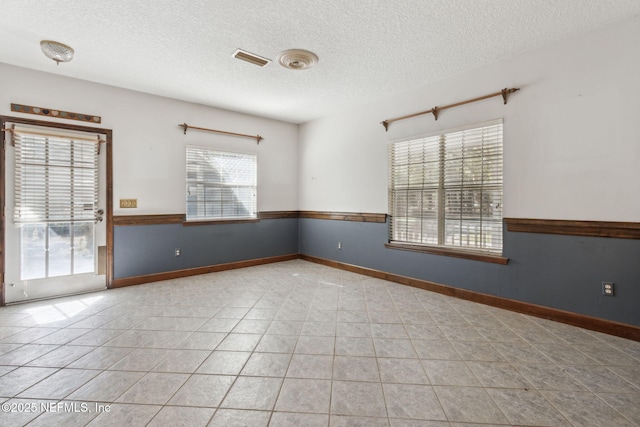 unfurnished room with tile patterned floors, visible vents, a textured ceiling, and baseboards