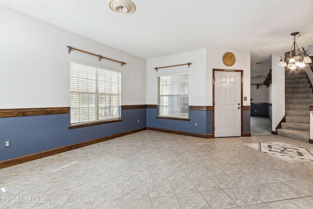 empty room featuring a textured ceiling, stairway, light tile patterned floors, baseboards, and wainscoting