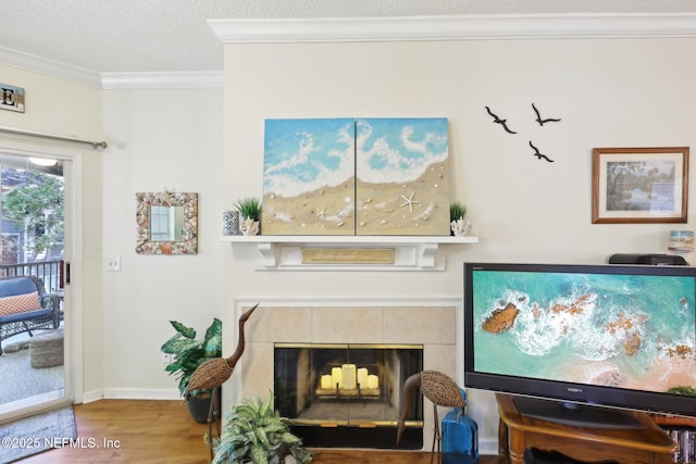 living room featuring a textured ceiling, wood finished floors, a fireplace, crown molding, and baseboards