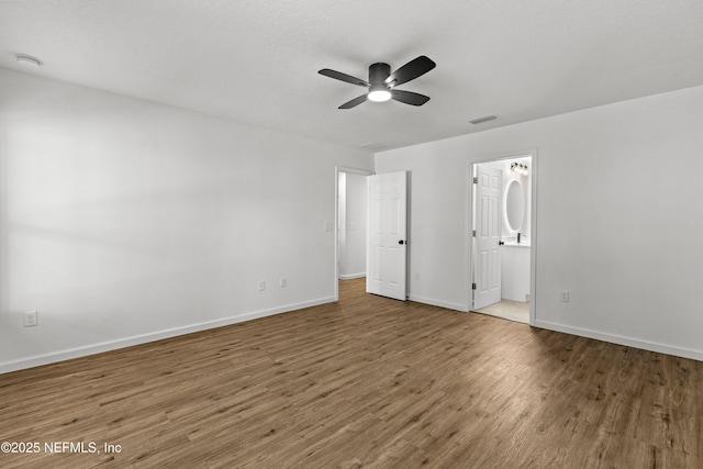 unfurnished bedroom with visible vents, ceiling fan, baseboards, wood finished floors, and ensuite bath