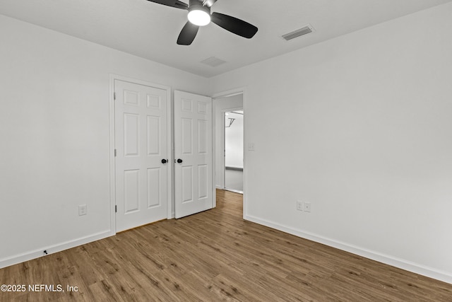 unfurnished bedroom featuring a ceiling fan, visible vents, wood finished floors, and baseboards