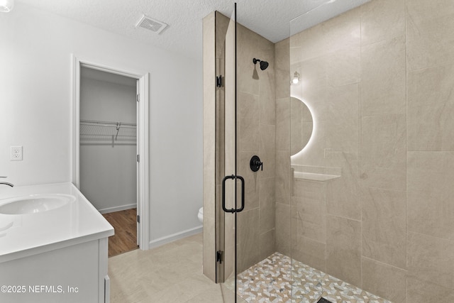 bathroom with visible vents, a shower stall, a walk in closet, a textured ceiling, and vanity