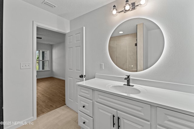 full bathroom with visible vents, a textured ceiling, wood finished floors, a tile shower, and vanity