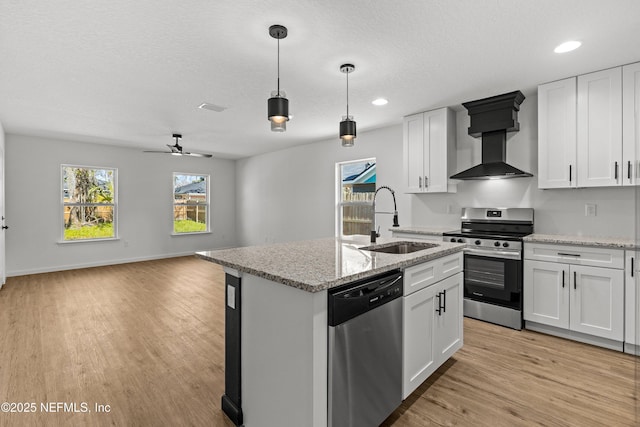 kitchen featuring a center island with sink, a sink, wall chimney range hood, appliances with stainless steel finishes, and light wood finished floors