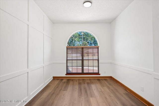 spare room featuring a textured ceiling, baseboards, and wood finished floors