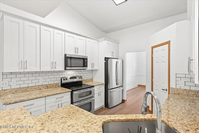 kitchen with light stone counters, decorative backsplash, appliances with stainless steel finishes, white cabinets, and a sink