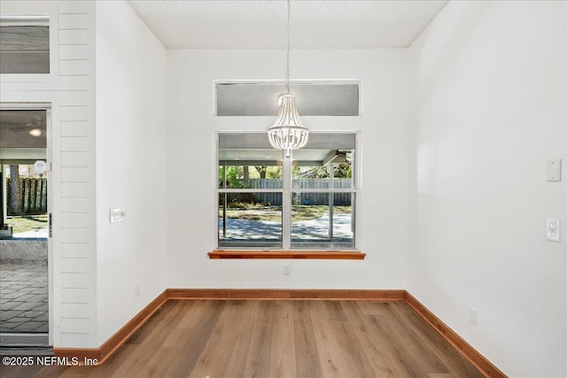 unfurnished dining area featuring a notable chandelier, a textured ceiling, baseboards, and wood finished floors