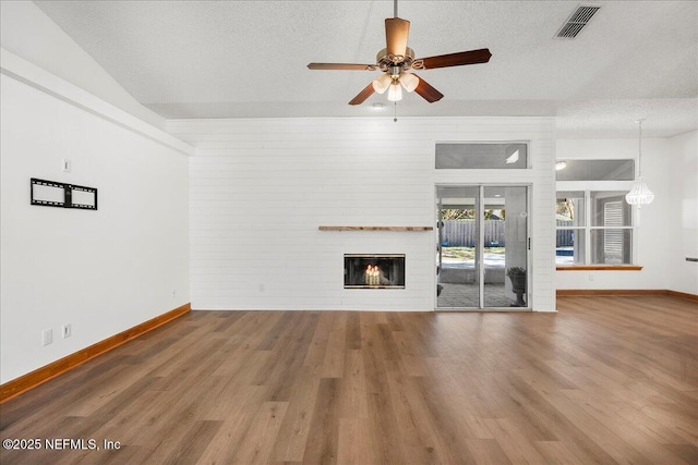 unfurnished living room featuring visible vents, a textured ceiling, a glass covered fireplace, and wood finished floors