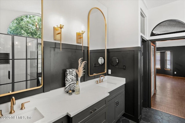 bathroom with double vanity, a wainscoted wall, tiled shower, and a sink