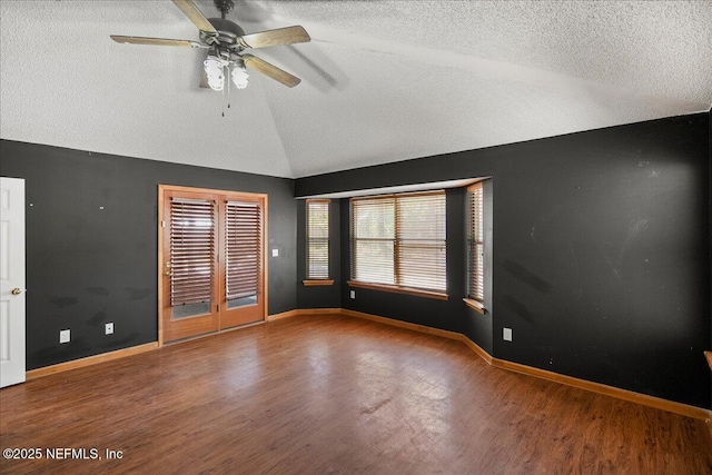 spare room with a textured ceiling, wood finished floors, baseboards, and vaulted ceiling