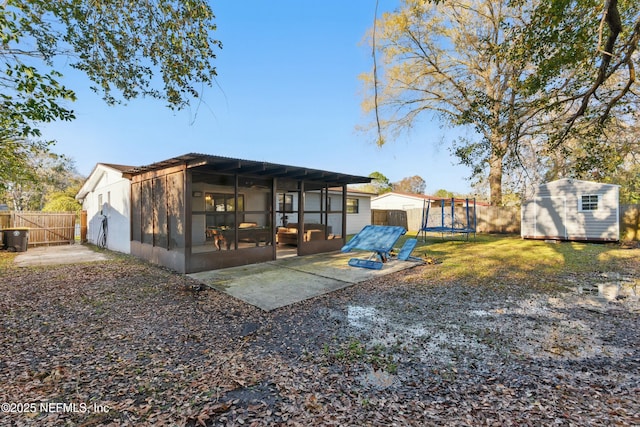 rear view of house with a trampoline, a shed, a sunroom, an outbuilding, and a patio