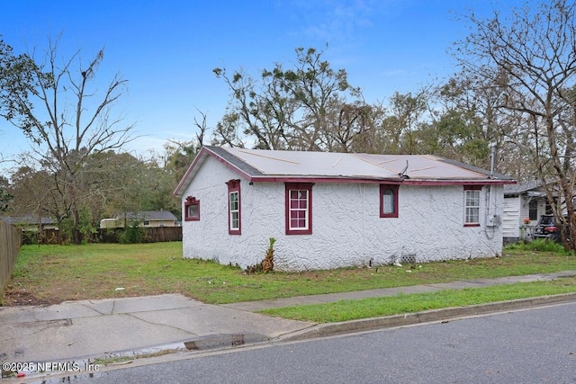 view of side of home with stucco siding, a lawn, and fence