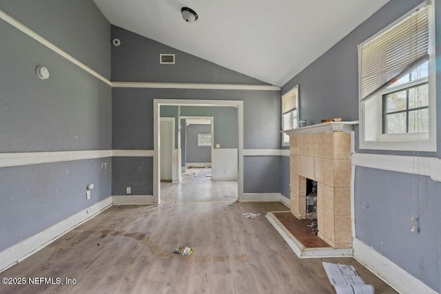 unfurnished living room with visible vents, baseboards, lofted ceiling, a tile fireplace, and wood finished floors