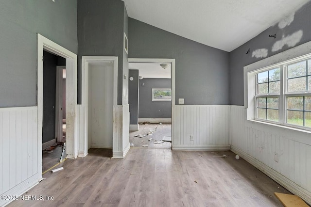 empty room with wainscoting, wood finished floors, and vaulted ceiling