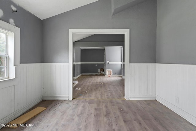 unfurnished room featuring wainscoting, wood finished floors, and vaulted ceiling