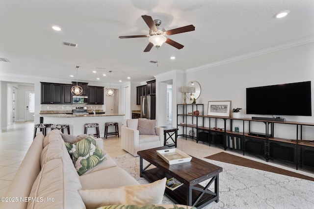 living room featuring light tile patterned floors, visible vents, ceiling fan, and crown molding