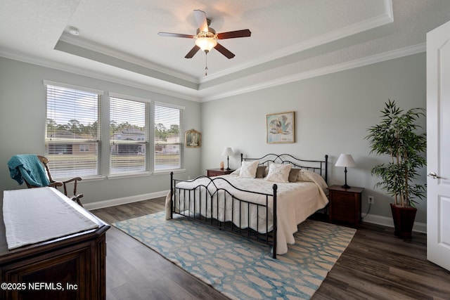 bedroom with dark wood-style floors, baseboards, a tray ceiling, and ornamental molding