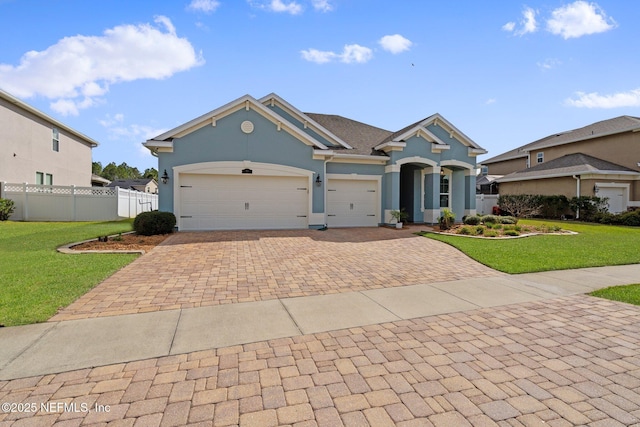 view of front facade featuring a front yard, fence, stucco siding, a garage, and decorative driveway