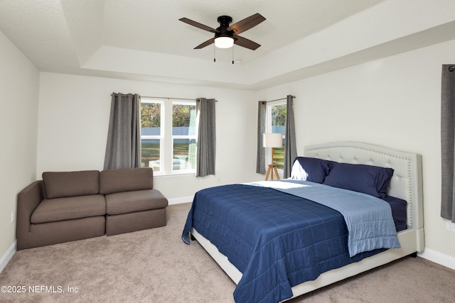 carpeted bedroom featuring a ceiling fan, a raised ceiling, and baseboards