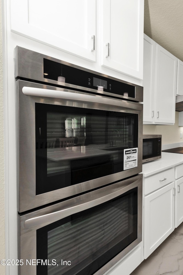 kitchen featuring stainless steel appliances, light countertops, white cabinets, under cabinet range hood, and marble finish floor